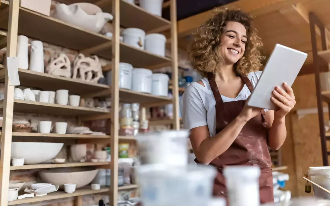 Femme entrepreneure souriante utilisant une tablette dans son magasin de poterie.