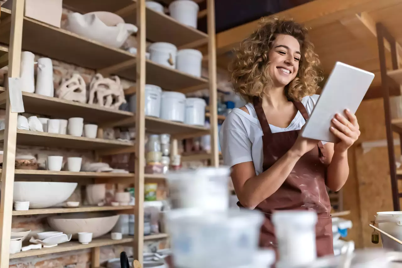 Femme entrepreneure souriante utilisant une tablette dans son magasin de poterie.